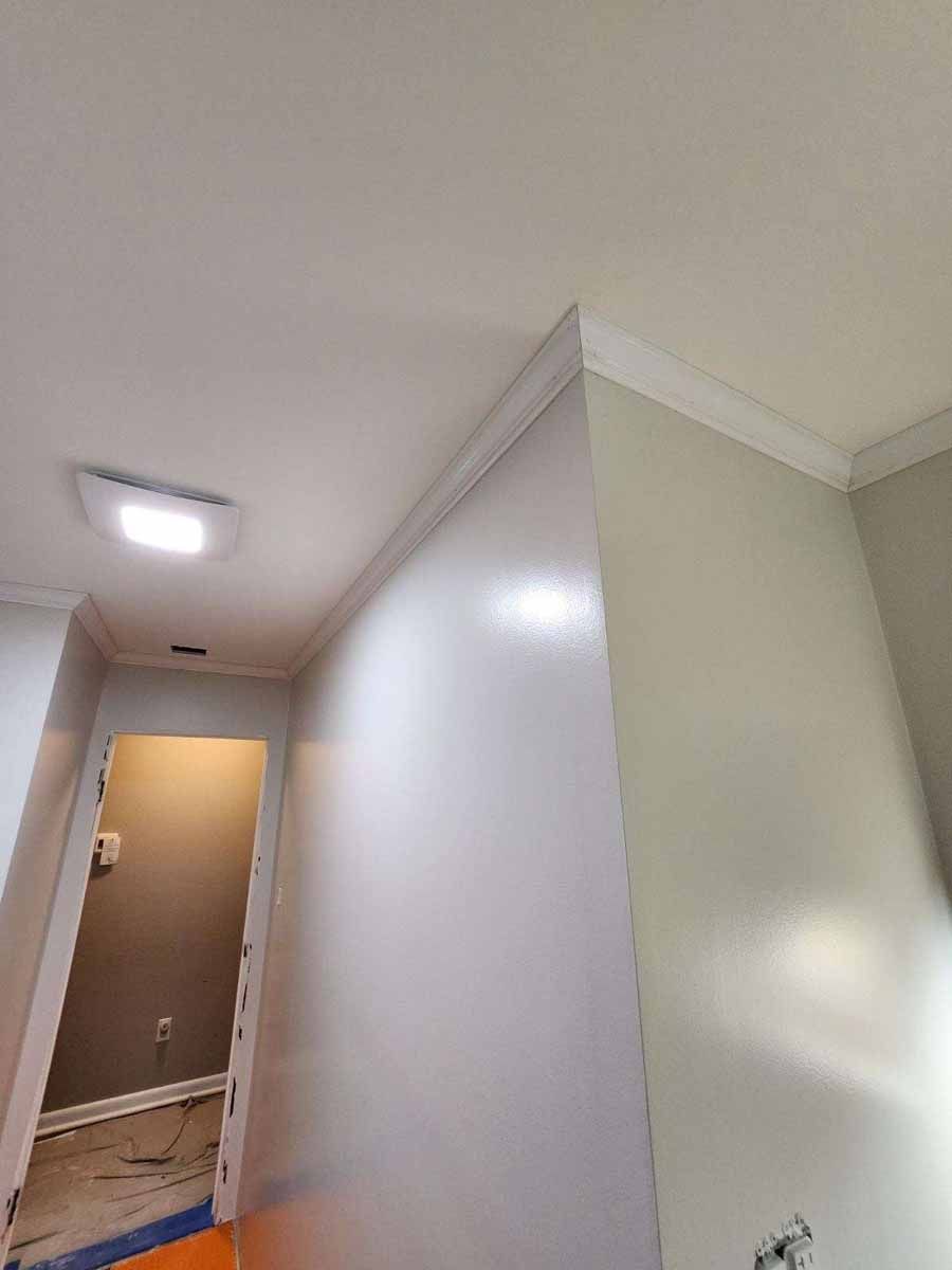 Interior corner with crown molding and a doorway. Walls are light gray, ceiling white. A light fixture is mounted.