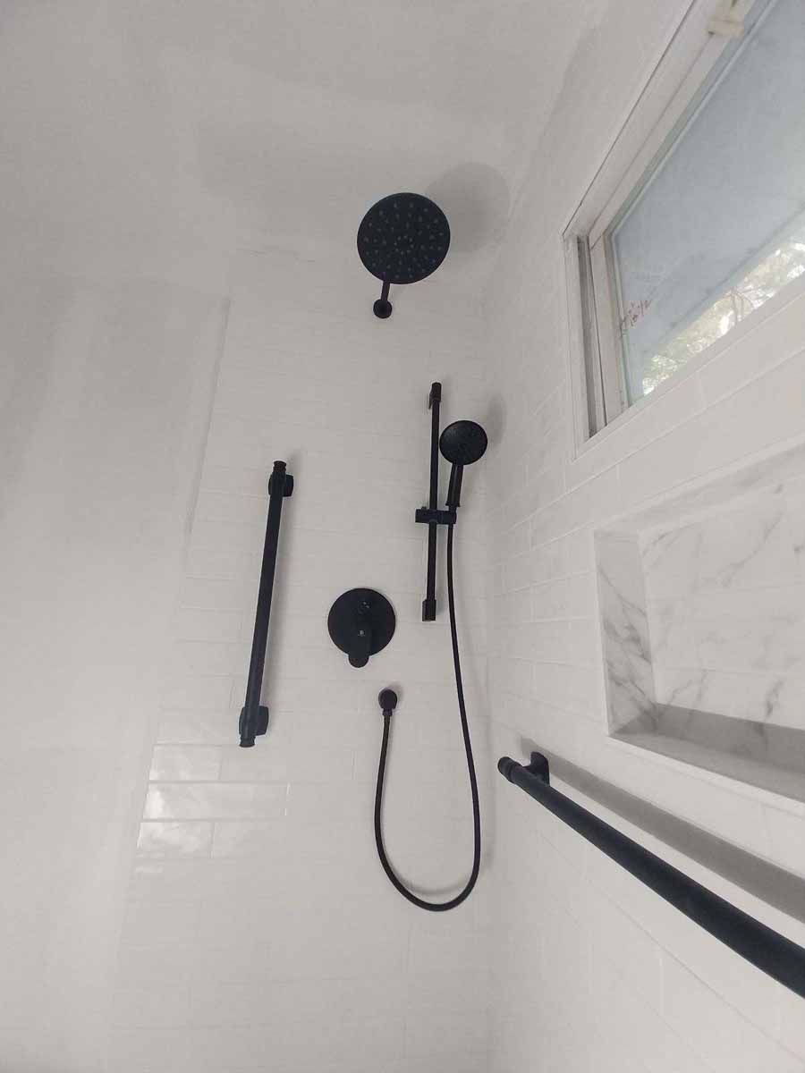 Black shower fixtures against white tiled wall with a small window.