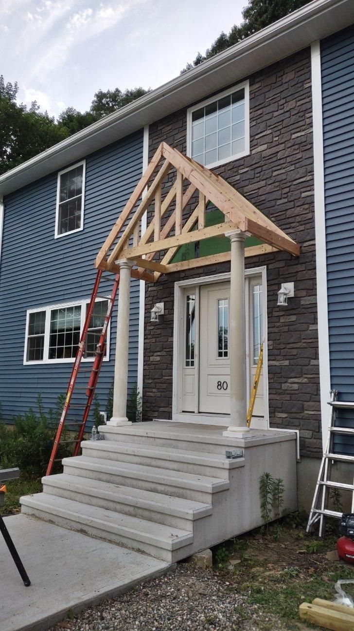 Two-story house with blue and stone siding, gray steps, and a partially constructed entry canopy.
