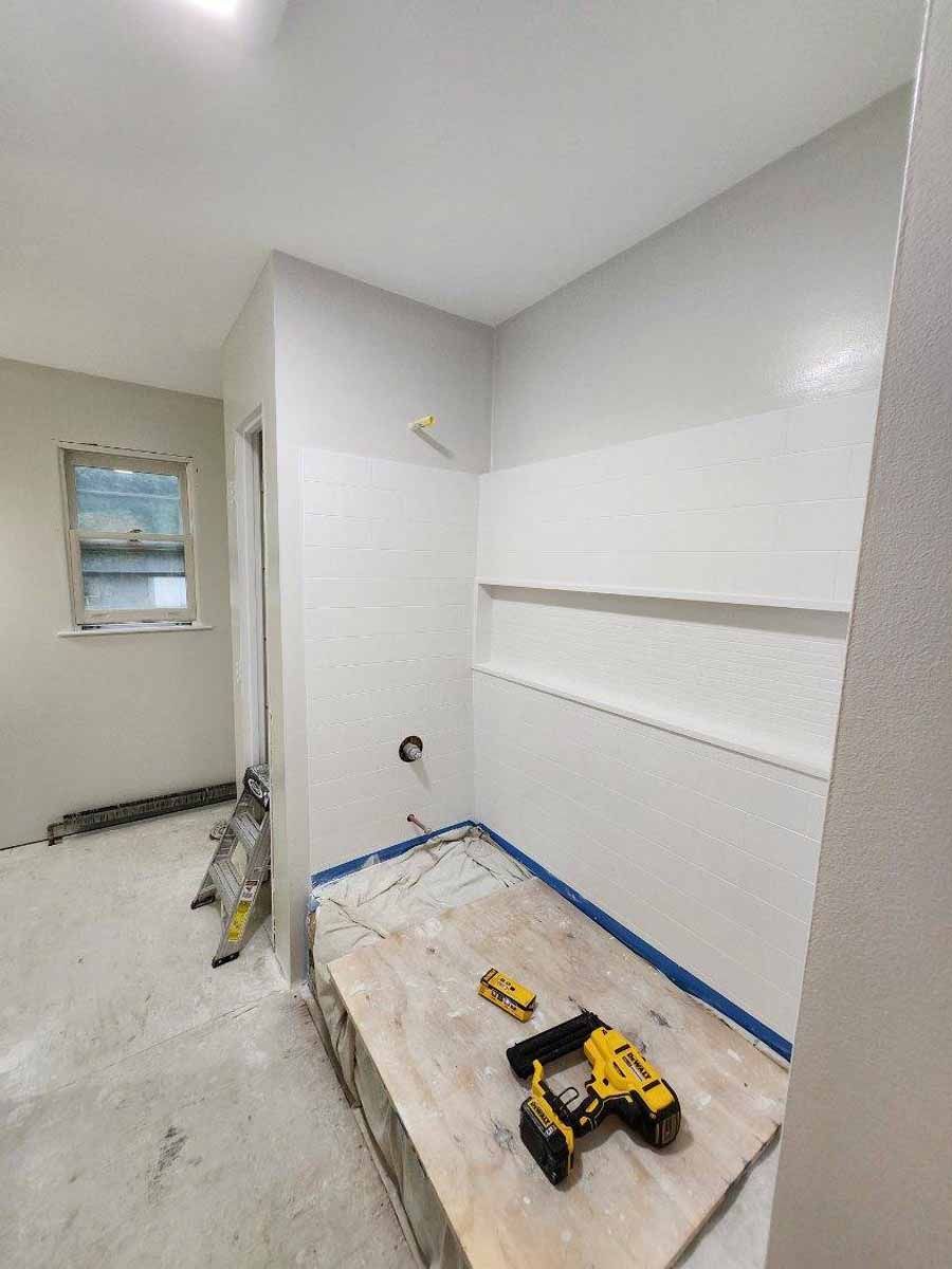 Bathroom under construction with white walls, window, and wood platform. Tools visible.