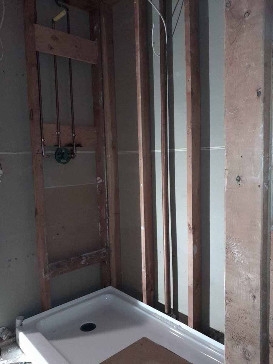 Framed-out shower stall with shower base installed. Plumbing visible. Studs are bare wood.