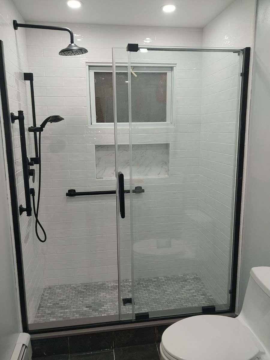 Modern bathroom with a glass shower enclosure, black fixtures, and white tiled walls.