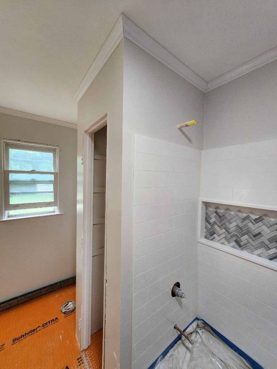 Bathroom under construction with white tile, gray walls, and window.