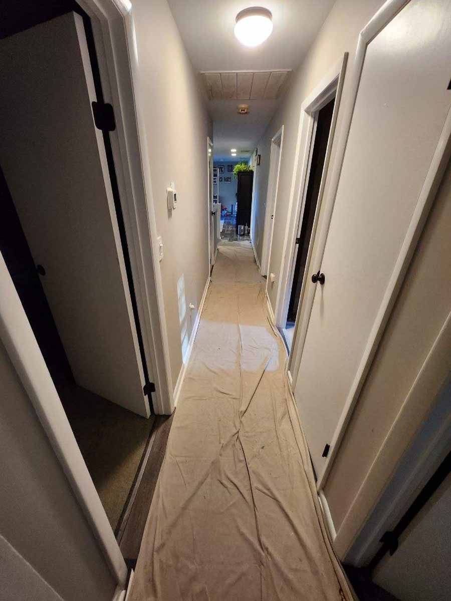 Narrow hallway with white doors, tan drop cloth on the floor, and a light fixture on the ceiling.
