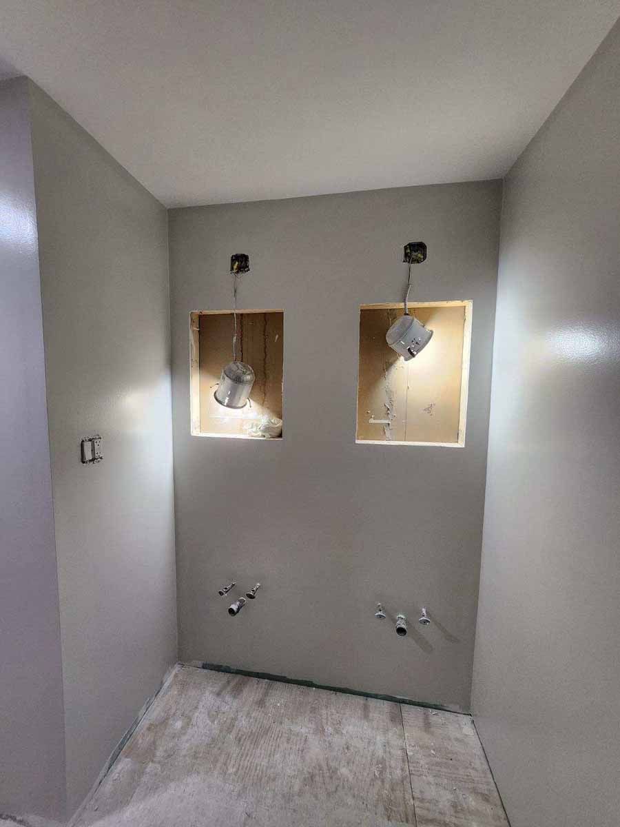 Bathroom under construction. Light gray walls, two recessed niches with exposed wiring, fixtures.