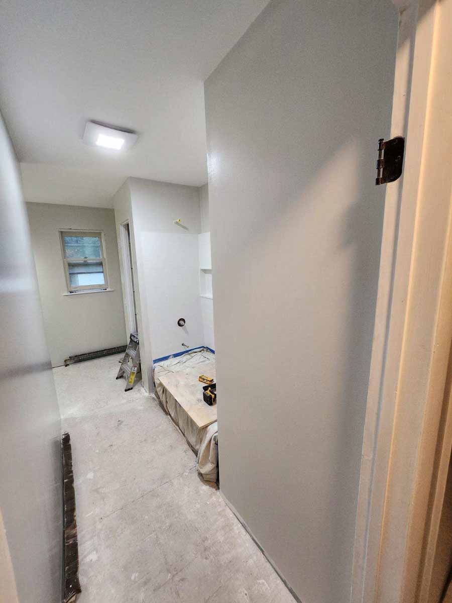 Bathroom under construction; light gray walls, open doorway, unfinished floor, window.