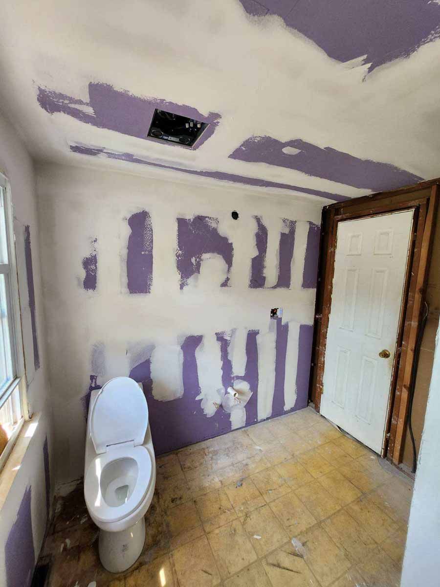 Bathroom under construction; drywall, toilet, and doorway visible. Purple drywall patches on white walls and ceiling.
