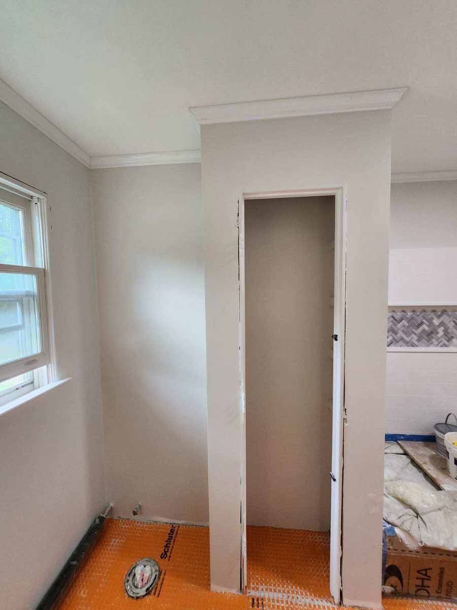 Empty closet doorway in a room with white walls, window, and orange flooring. Crown molding on ceiling.