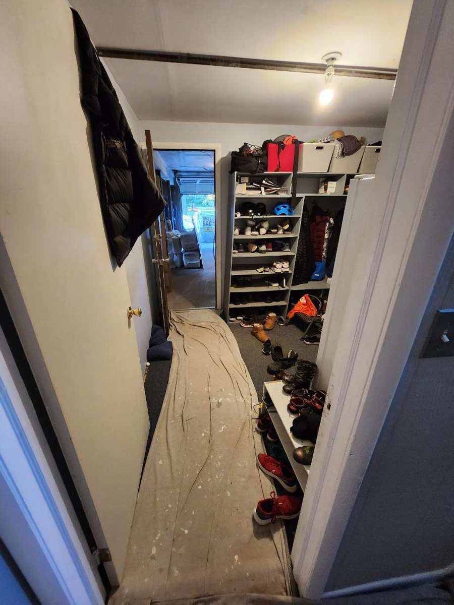 Narrow hallway with concrete floor, shoe racks, and open doorway to an outside area.