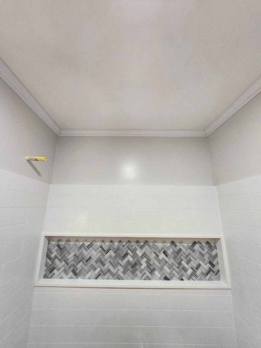 White bathroom wall with a built-in recessed area featuring a gray and white herringbone tile pattern.