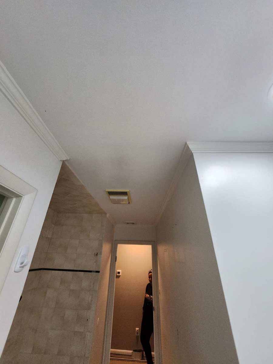 Narrow hallway with a person standing in the doorway, white ceiling and walls, beige tiled wall.