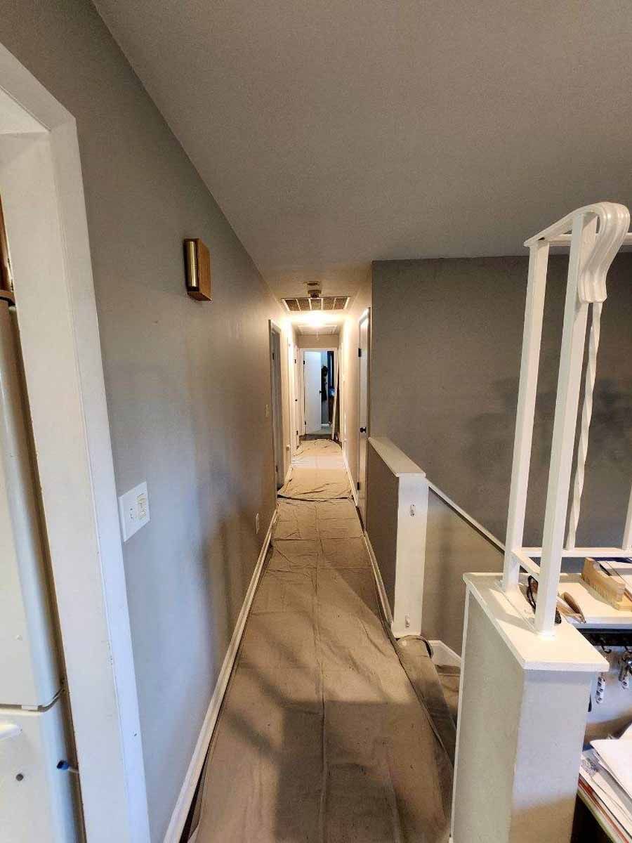 Narrow hallway with gray walls, white trim, and a partially covered floor. A doorway is visible at the end.