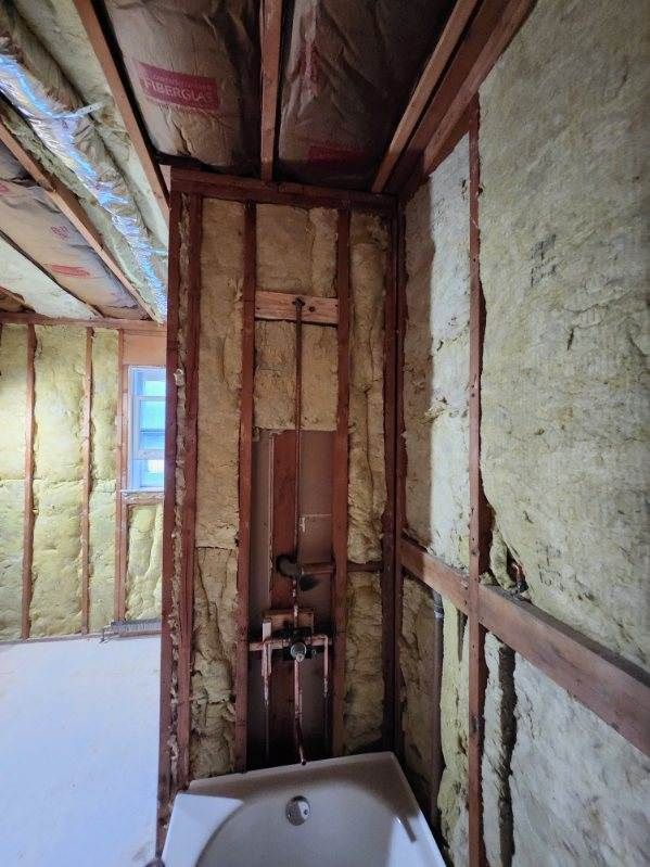 Bathroom under construction: Framing, insulation, copper pipes, and a bathtub are visible.