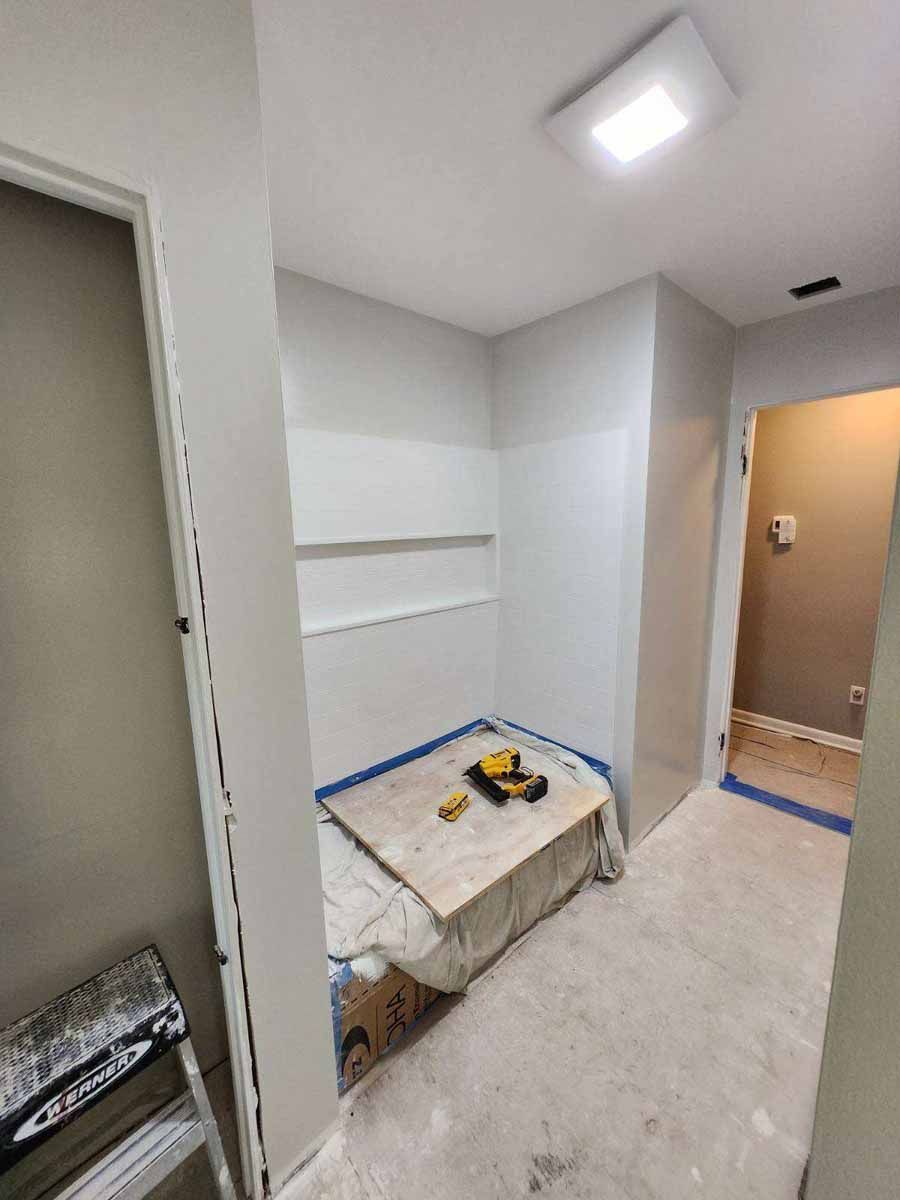 Interior view of a small room under construction, with painted walls, shelves, and a covered surface holding tools.