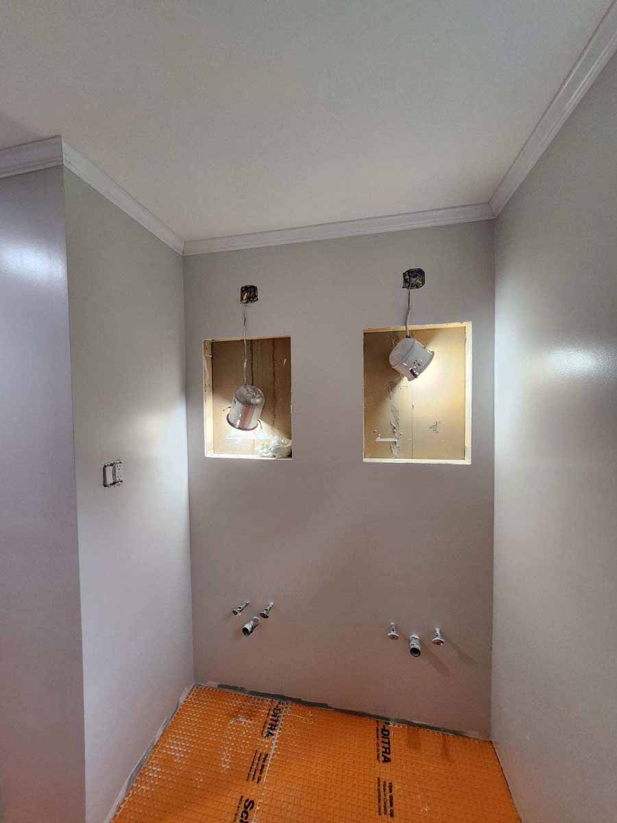 Bathroom under construction with two wall niches, unfinished plumbing, and orange floor membrane.