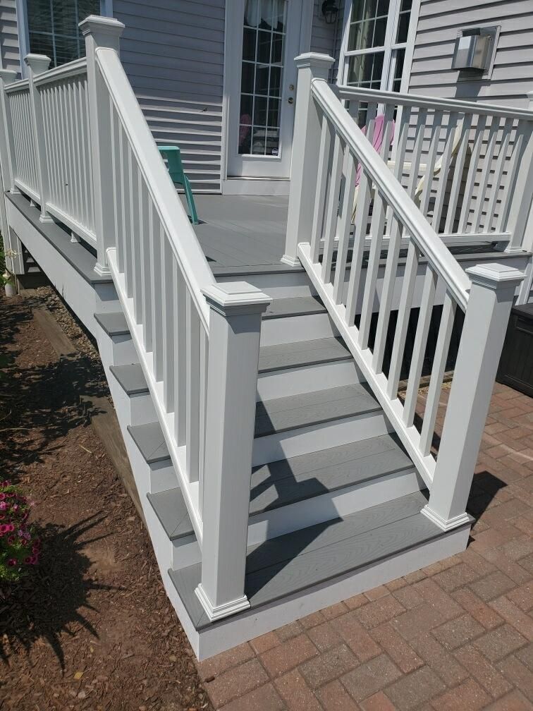 White railing, gray steps leading up to a deck, brick patio.