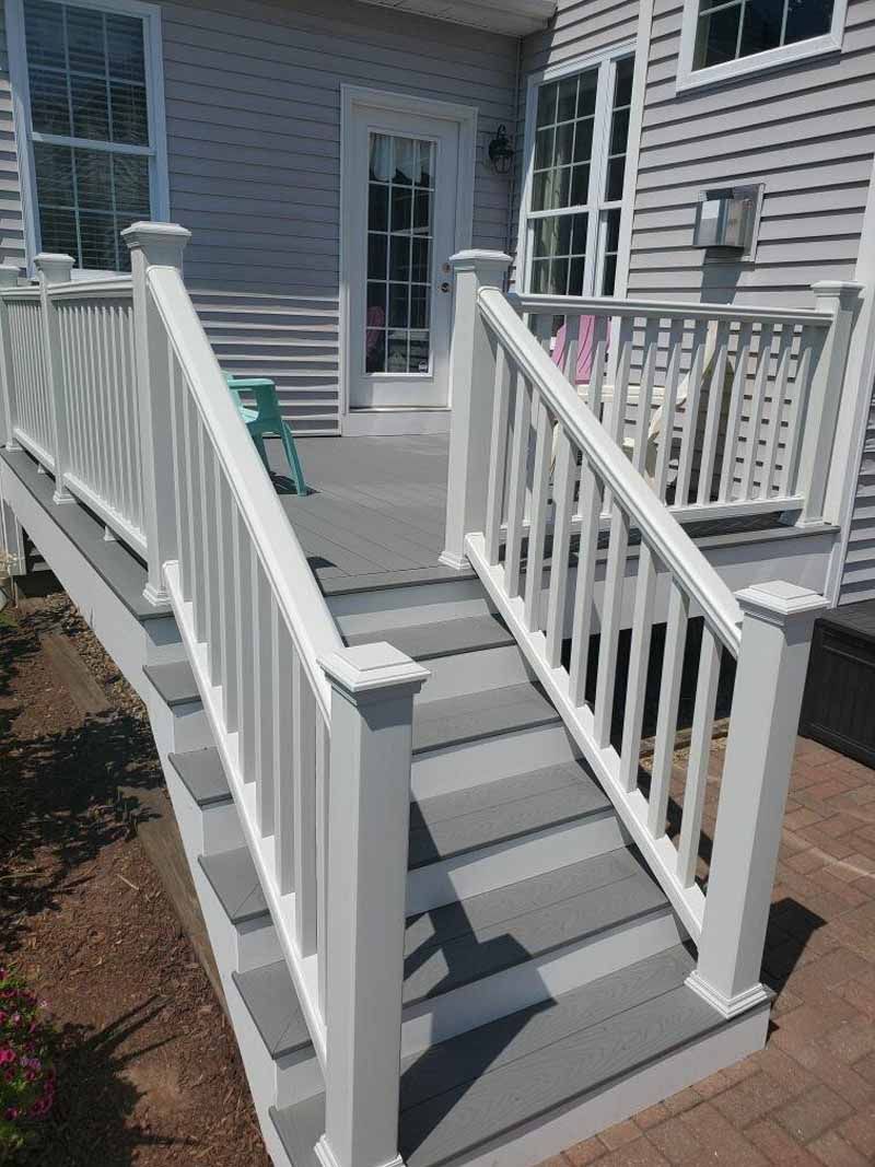 Gray and white deck with stairs, railing, and a door to a house.