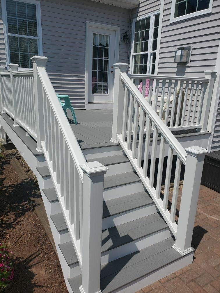 White railing and steps leading up to a gray deck attached to a light gray house.