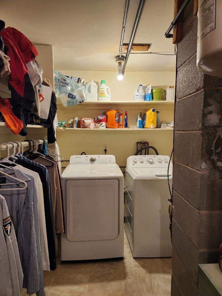 Laundry room with white washer and dryer, shelves with supplies, and hanging clothes.