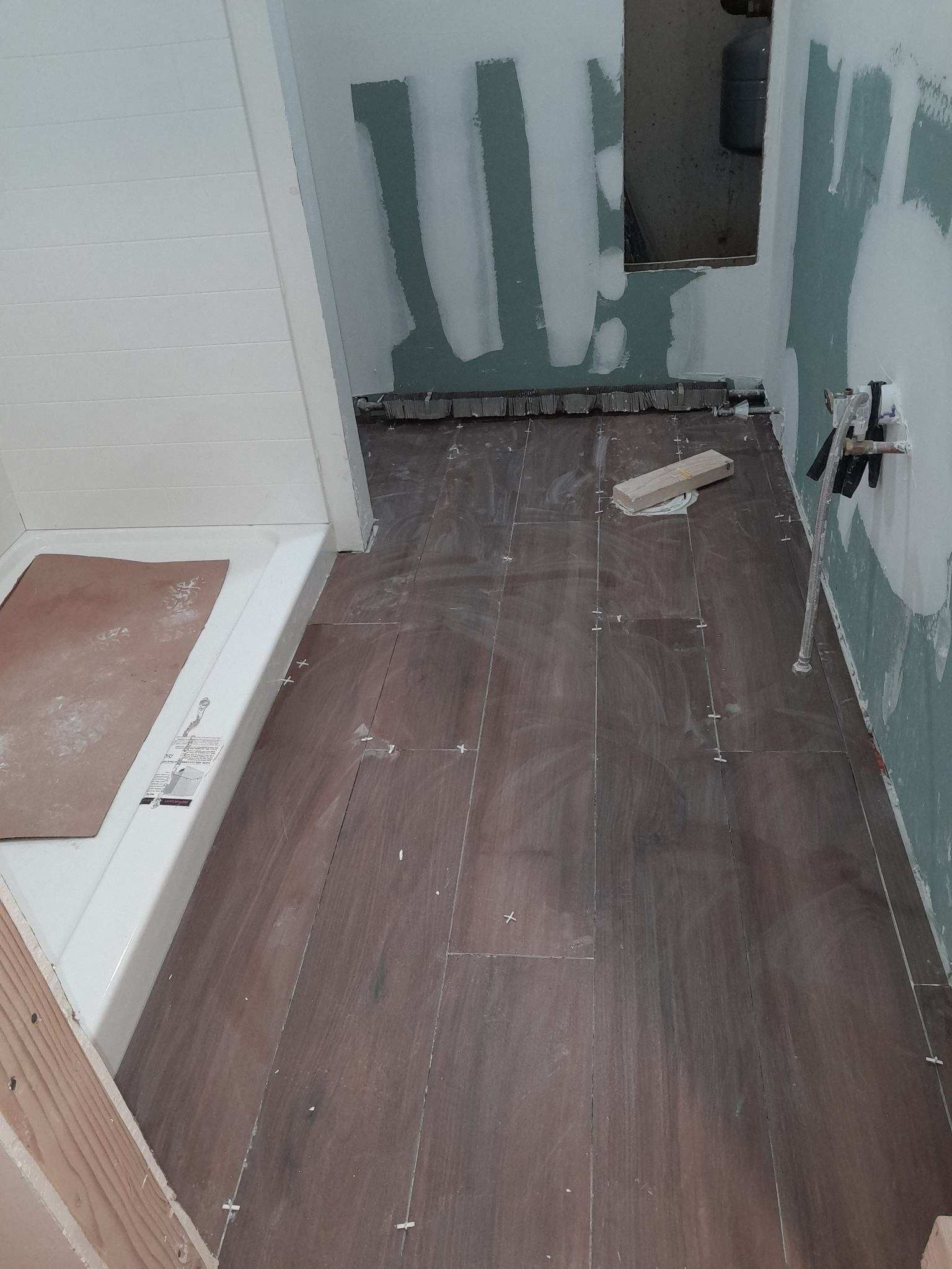 Bathroom under construction with brown floorboards, white shower base, and partially finished walls.
