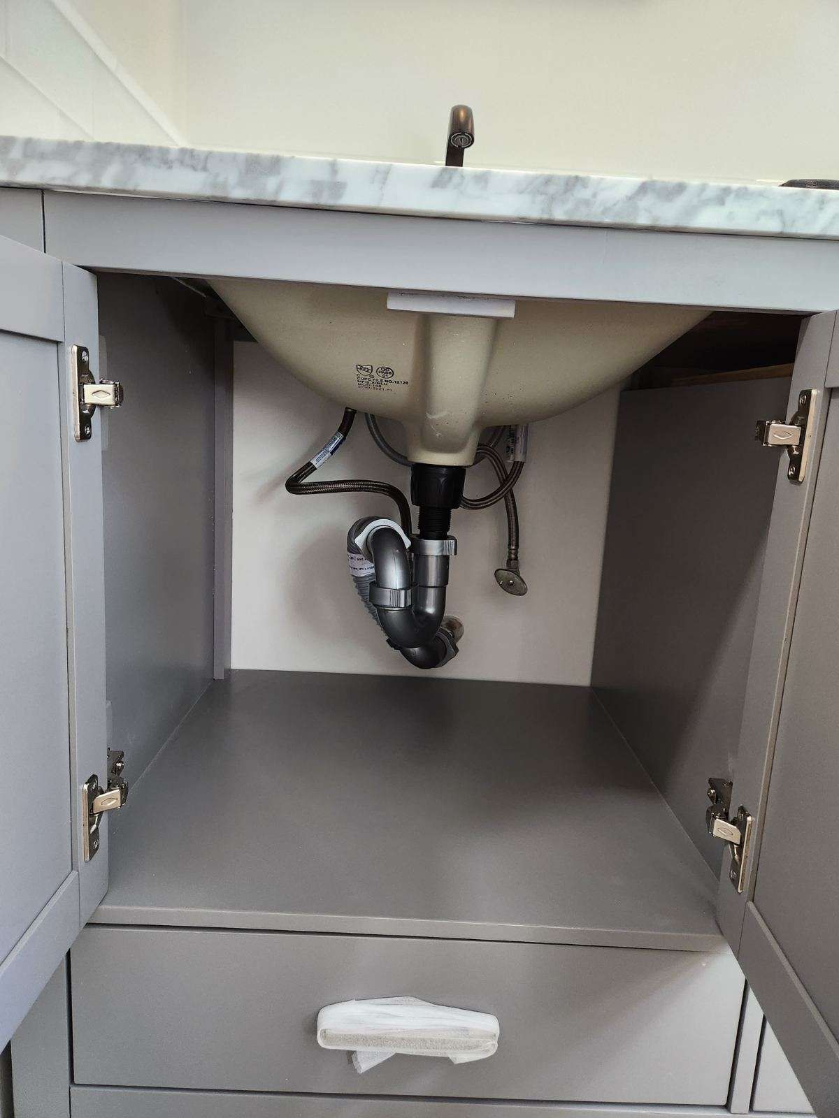 Gray bathroom vanity with open doors, showing sink basin, plumbing, and a drawer.