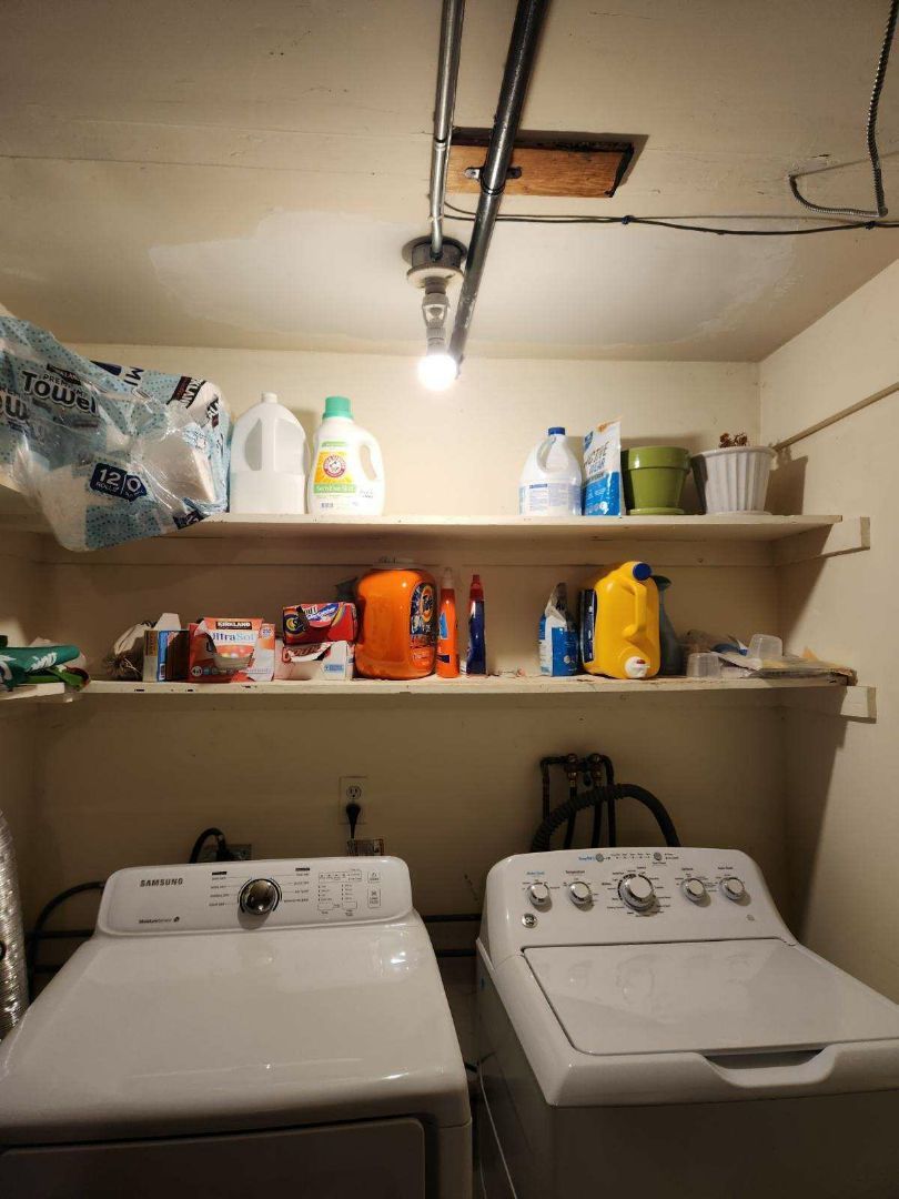 Laundry room with white washer and dryer, shelves with supplies, and overhead light.