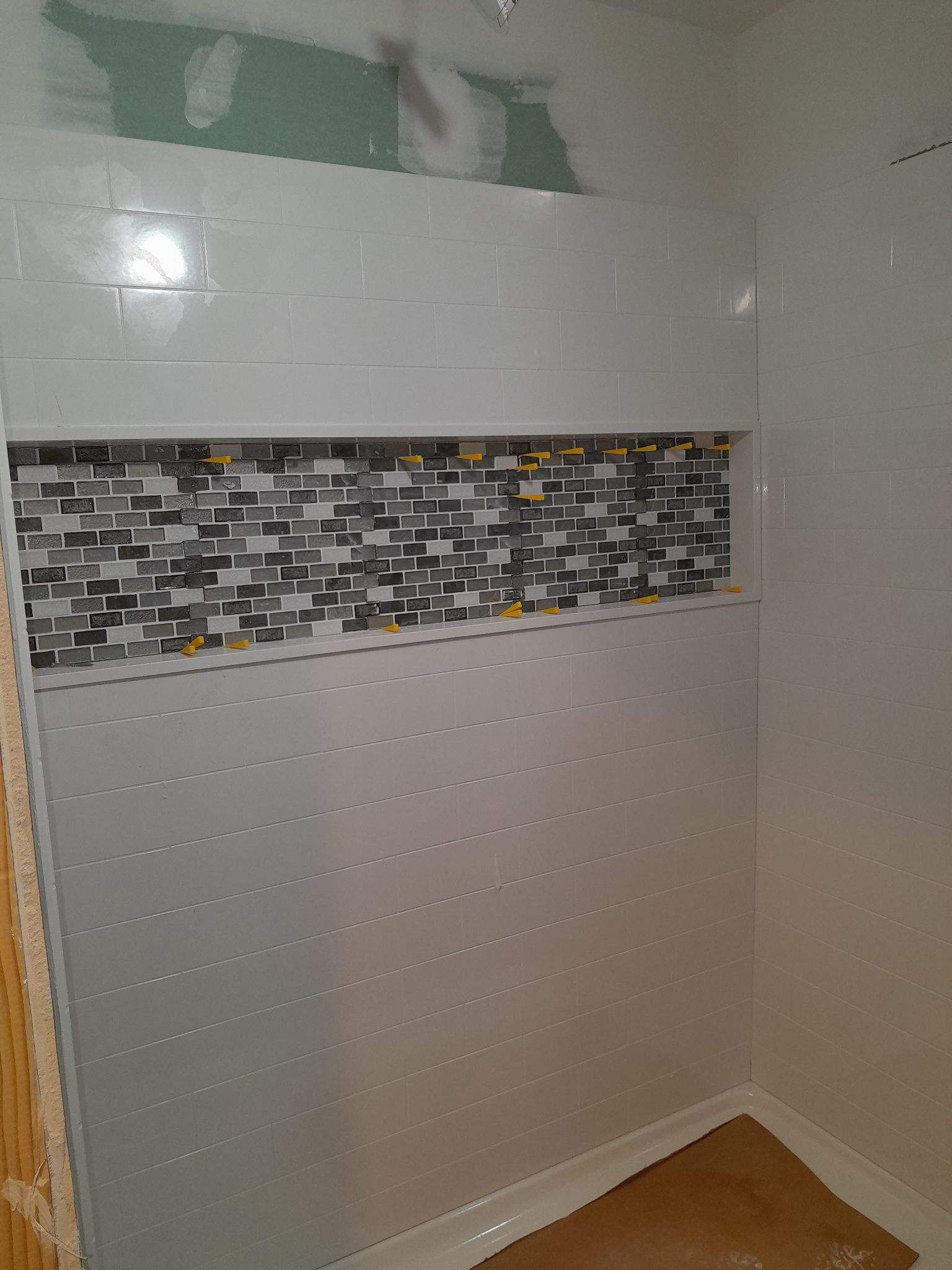 Shower with white tile and a mosaic tile accent in the recessed shelf.