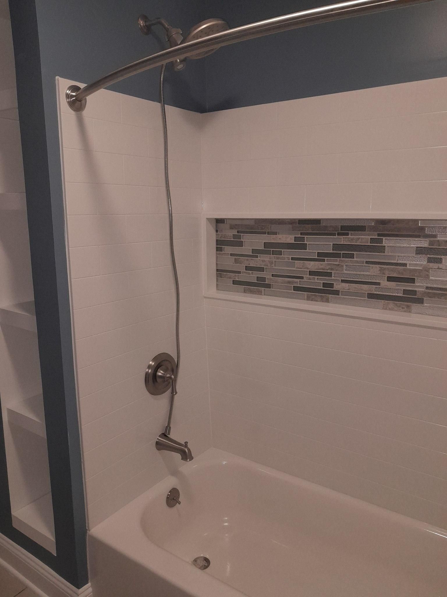 Shower with white walls and tub, blue upper wall, and decorative tiled niche.
