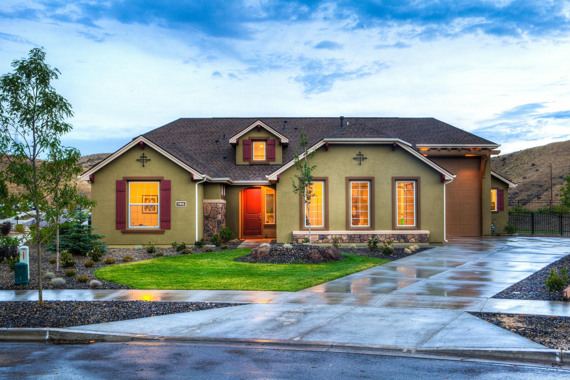 Single-story home with tan exterior, red door, and driveway reflecting cloudy sky.