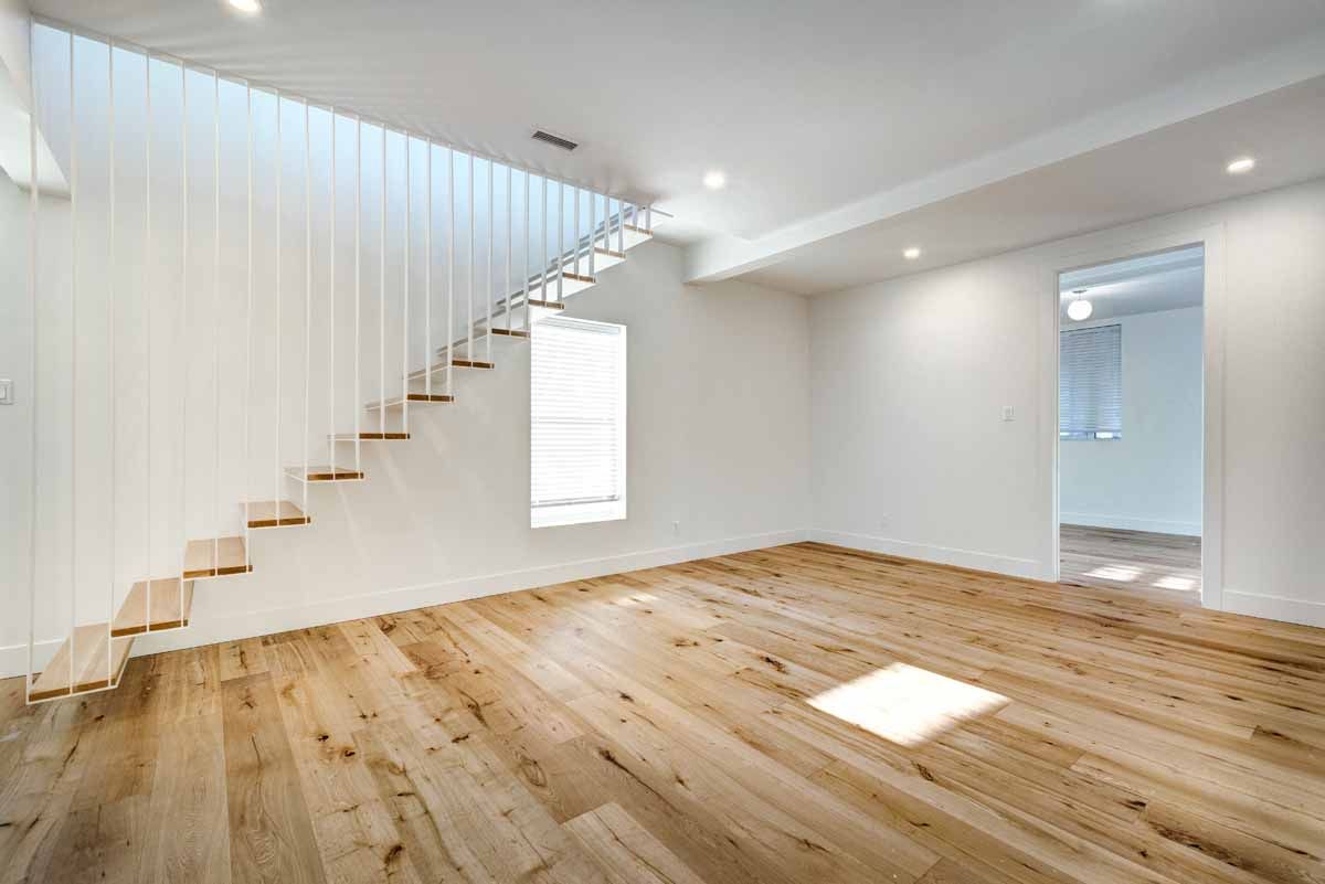 Empty room with wooden floor, stairs, white walls, and bright sunlight.