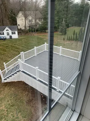 White deck with gray flooring, railing, and stairs, viewed from a window. Houses and trees are in the background.