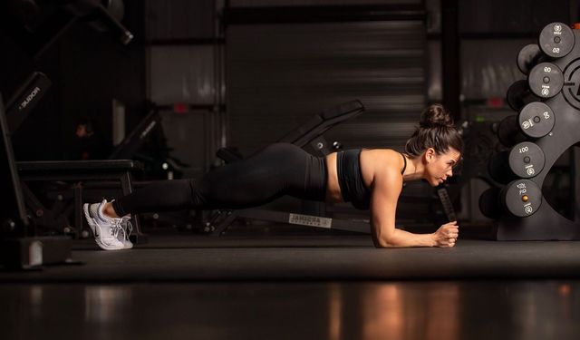 A woman is doing a plank on the floor in a gym.