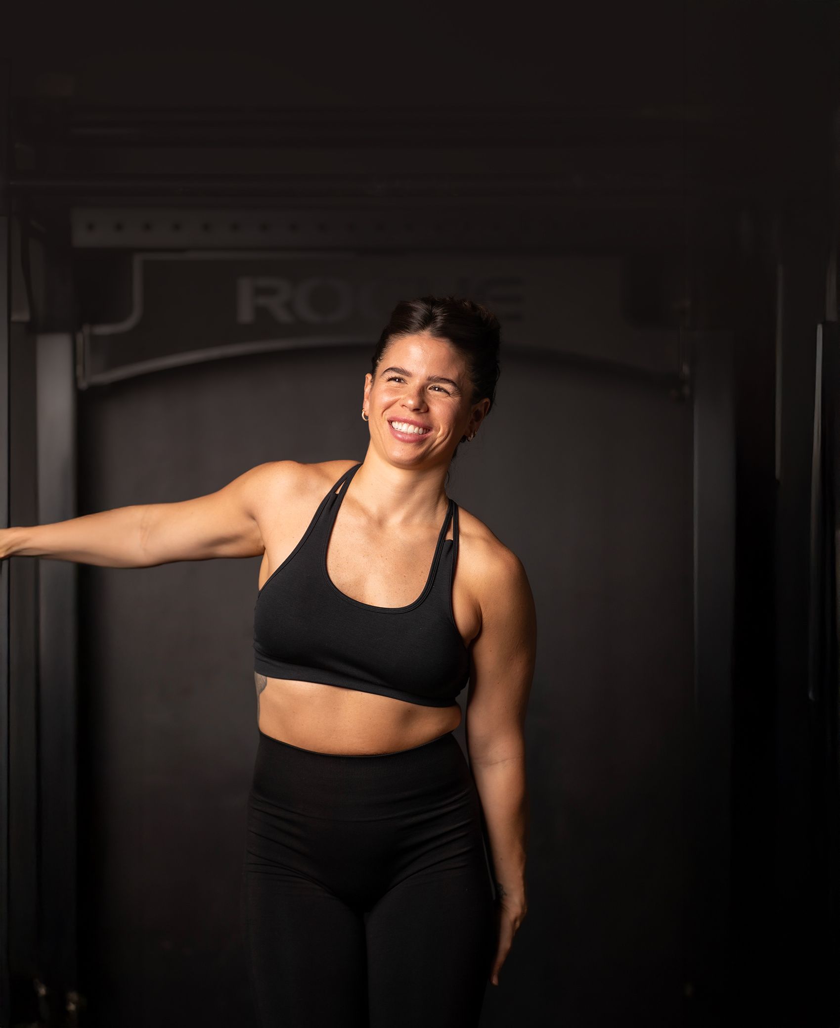 A woman in a black sports bra and black pants is standing in front of a door.