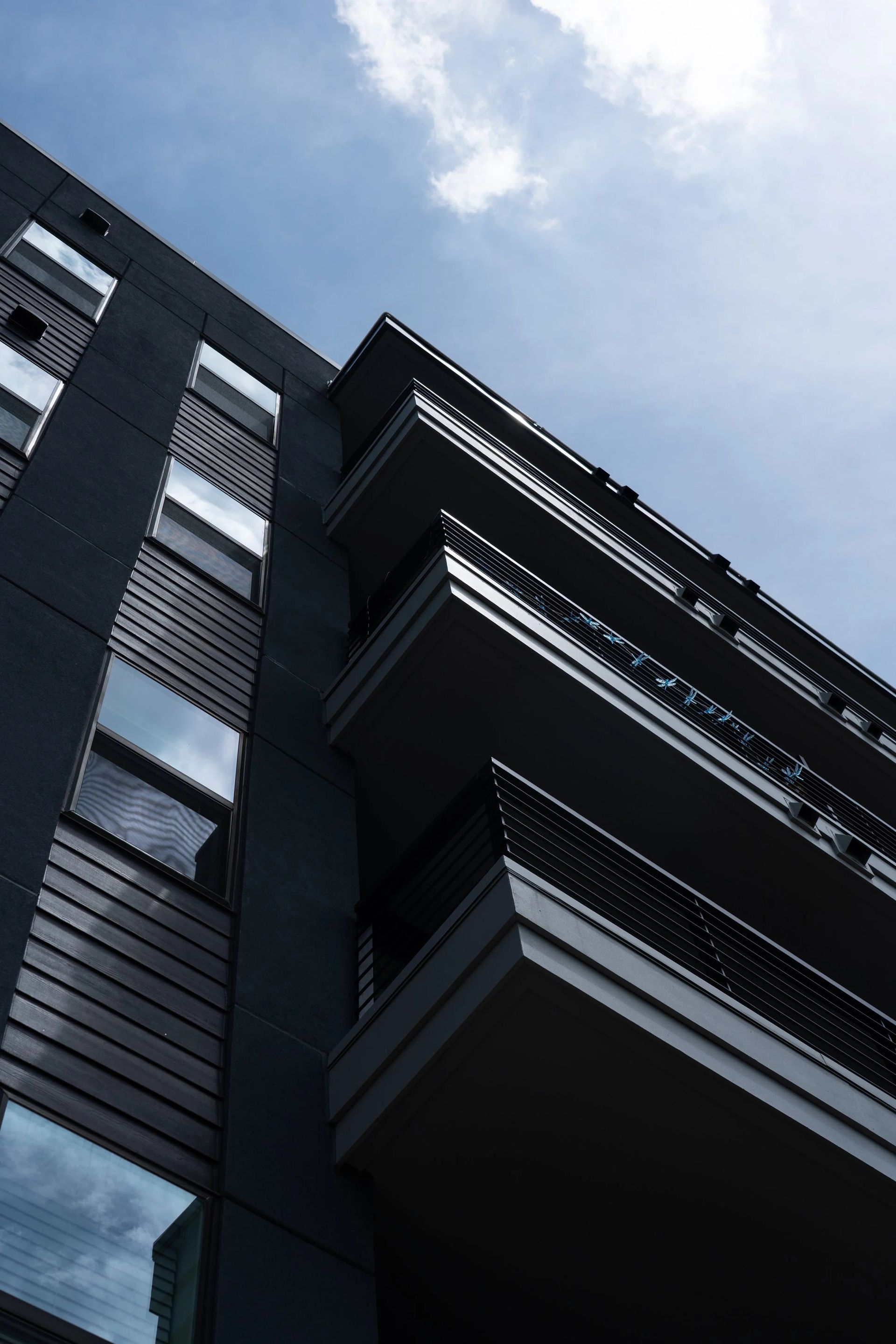 Modern dark gray building with balconies against a blue sky with clouds.