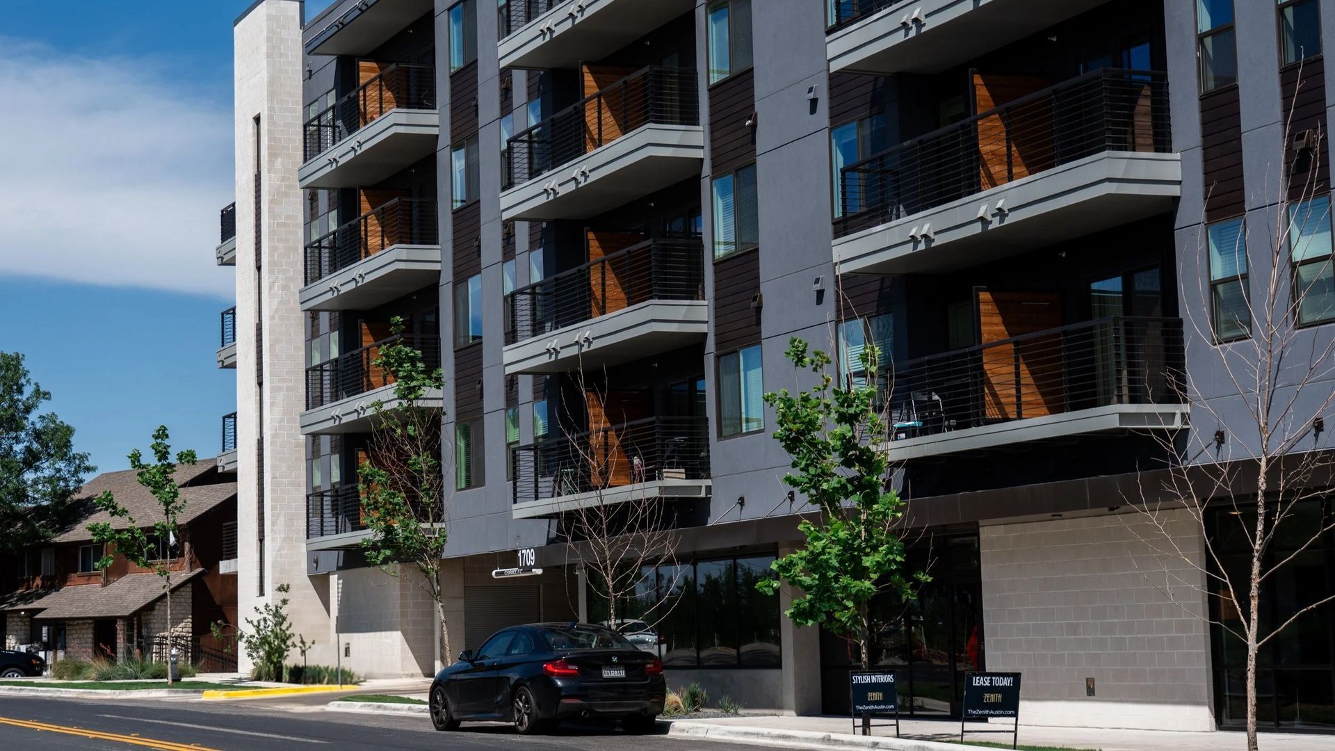 Modern apartment building with balconies, a parked car, and trees.