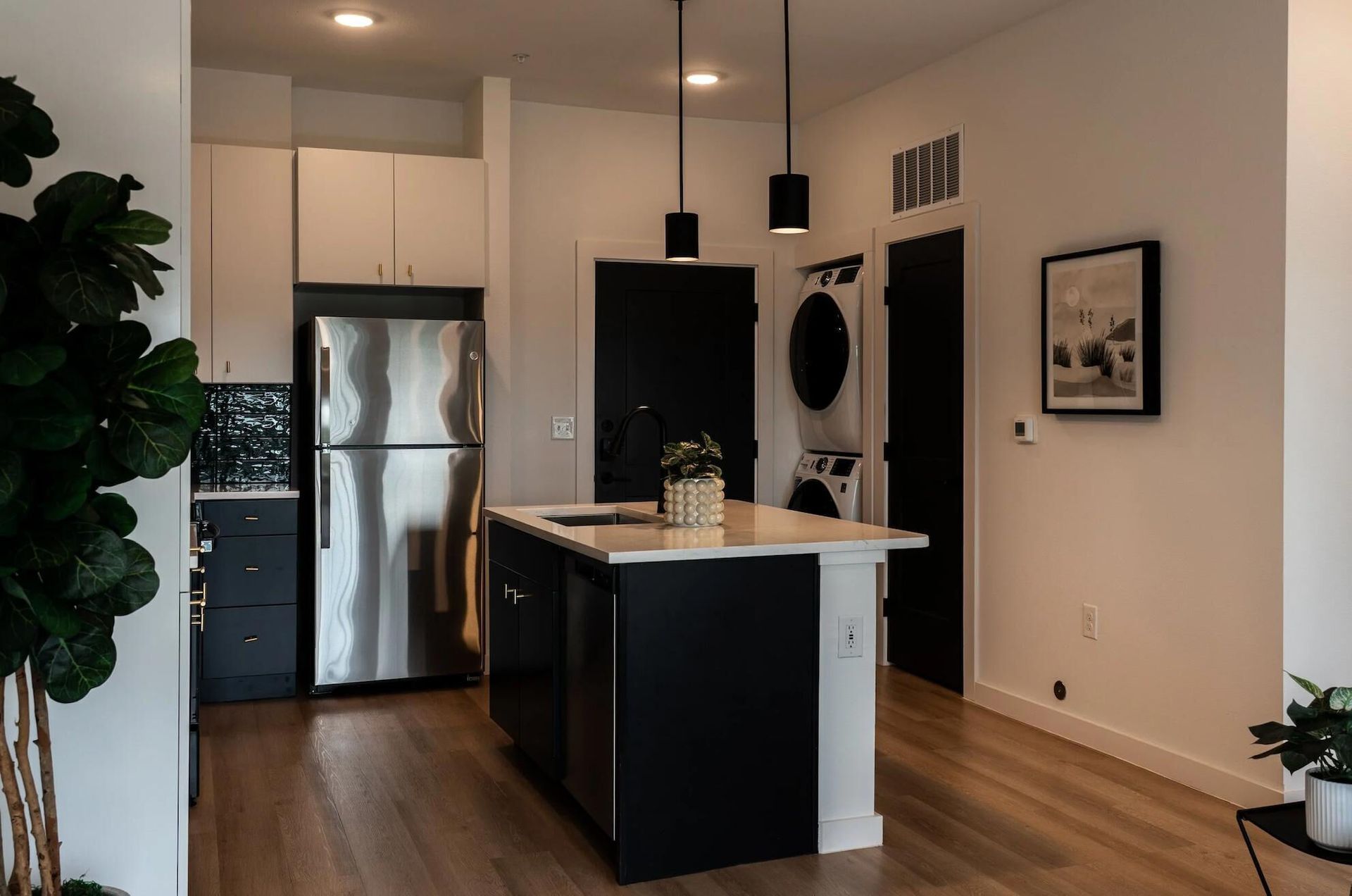 Modern kitchen with island, stainless steel appliances, black and white cabinets, and wooden floors.