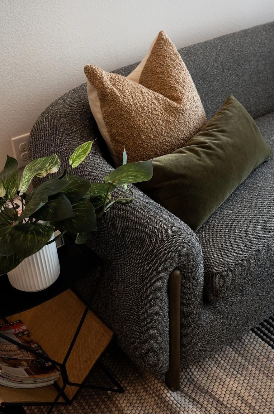 Gray sofa with tan and green pillows, next to a small side table with a plant.