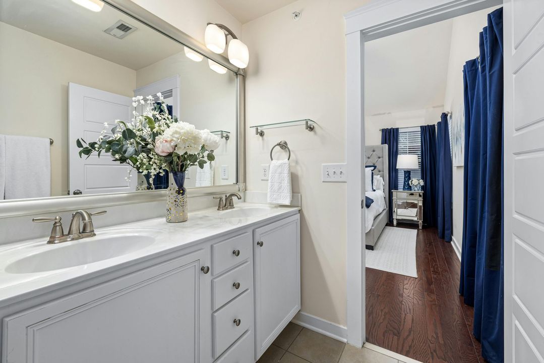 A bathroom with two sinks , a mirror and a vase of flowers.