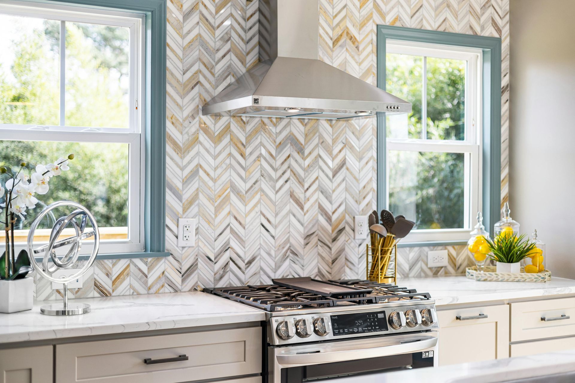 A kitchen with a stove , oven , sink , and two windows.