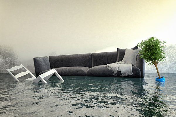 A living room is flooded with water and a couch and chair are floating in the water.