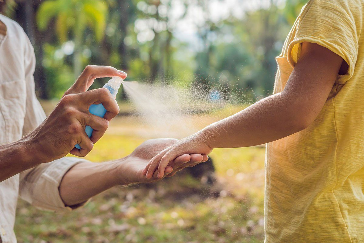 A person is spraying insect repellent on a child 's arm.