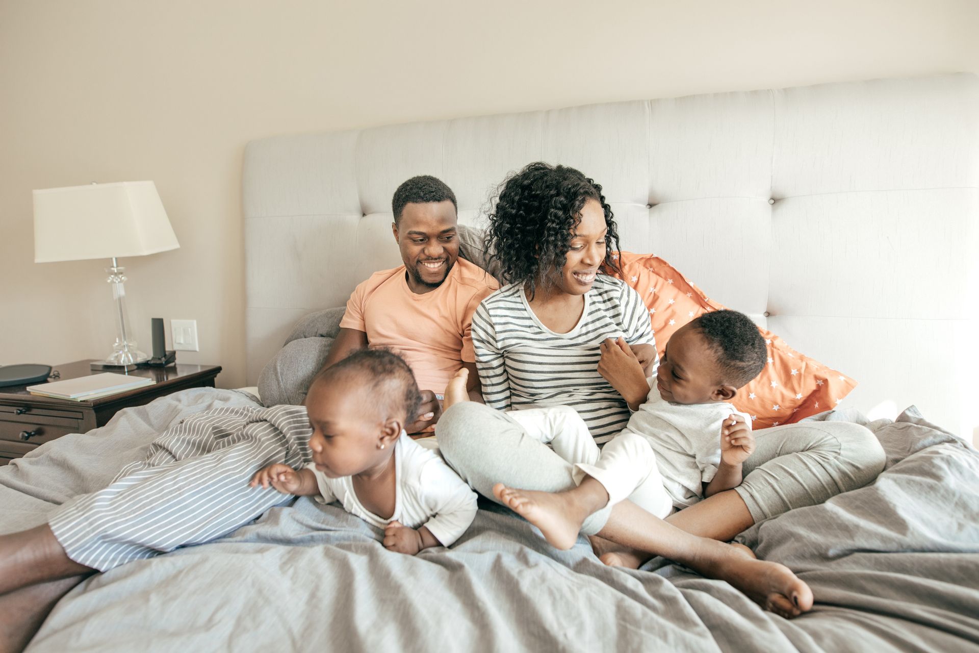 A family is sitting on a bed playing with their children.