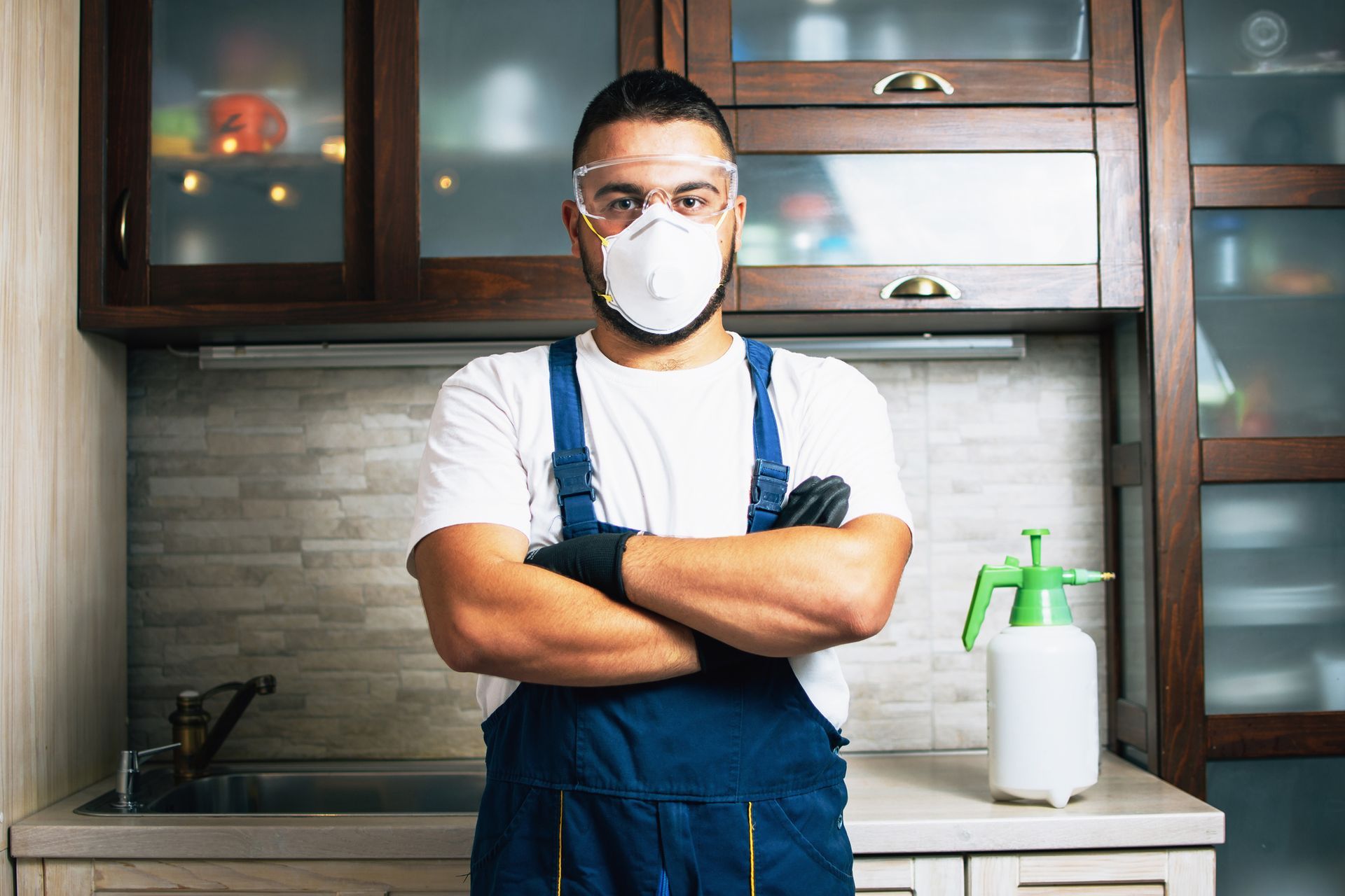 A pest control technician is standing in a kitchen with his arms crossed.