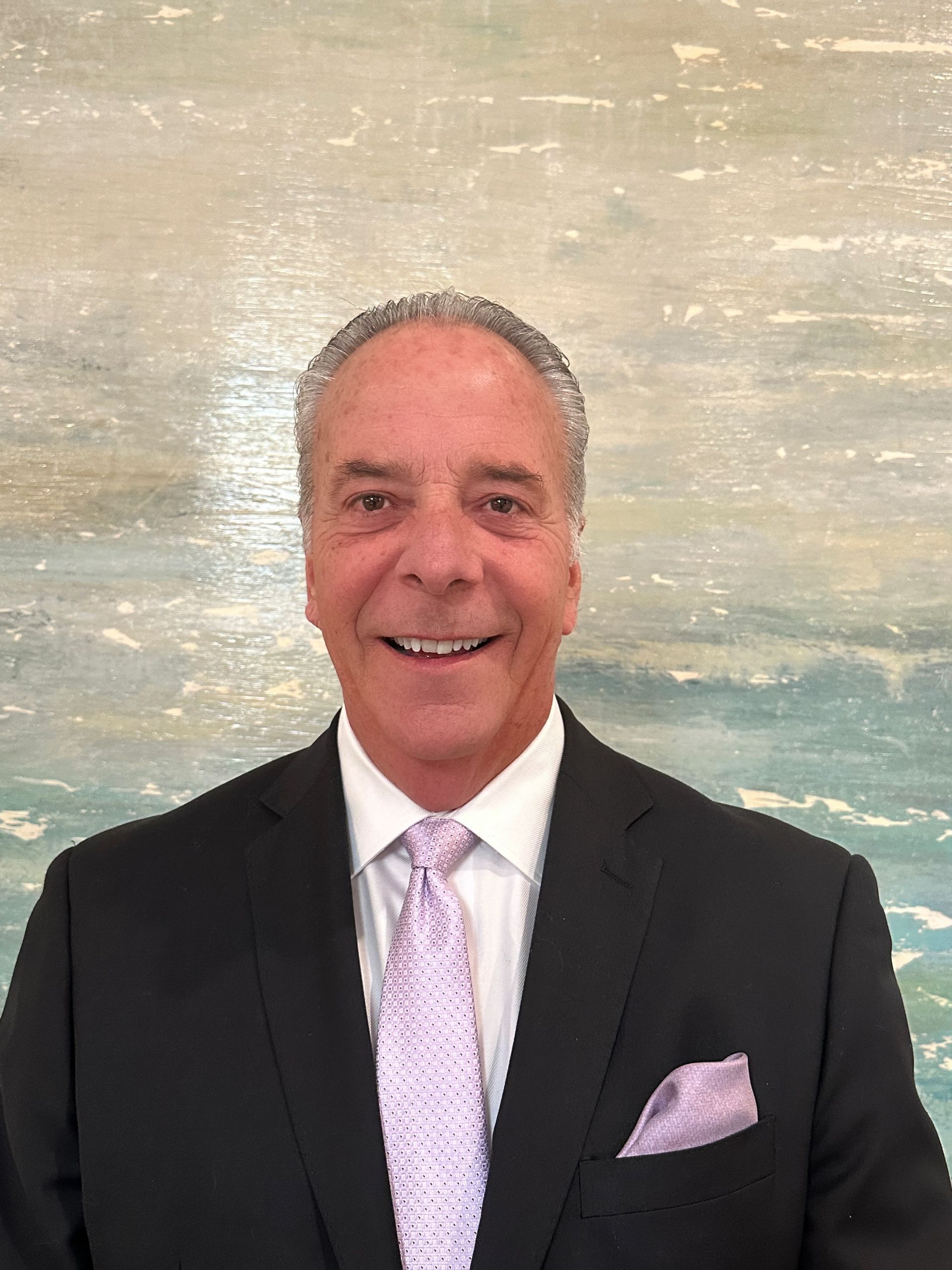 A man in a suit and tie is smiling in front of a painting.