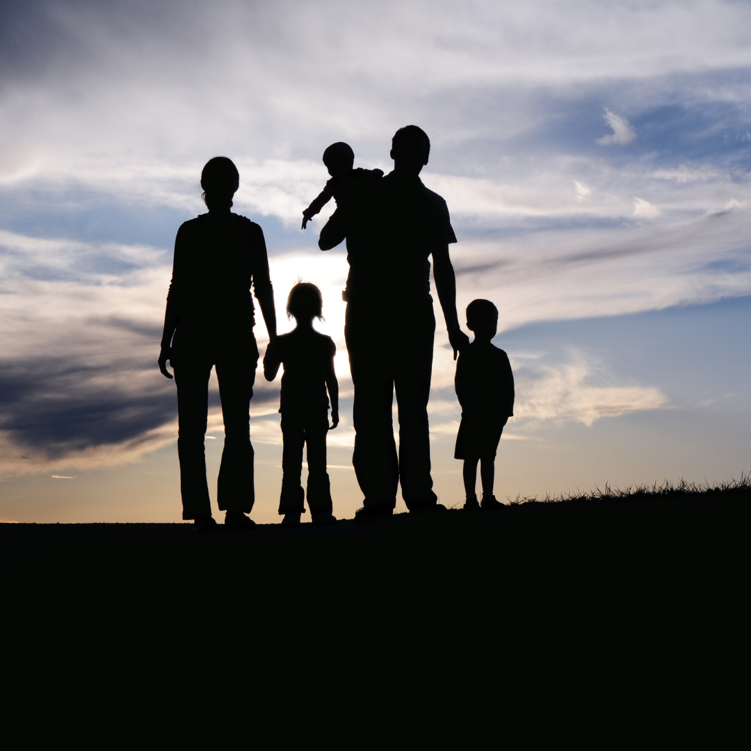 A silhouette of a family standing on a hill at sunset