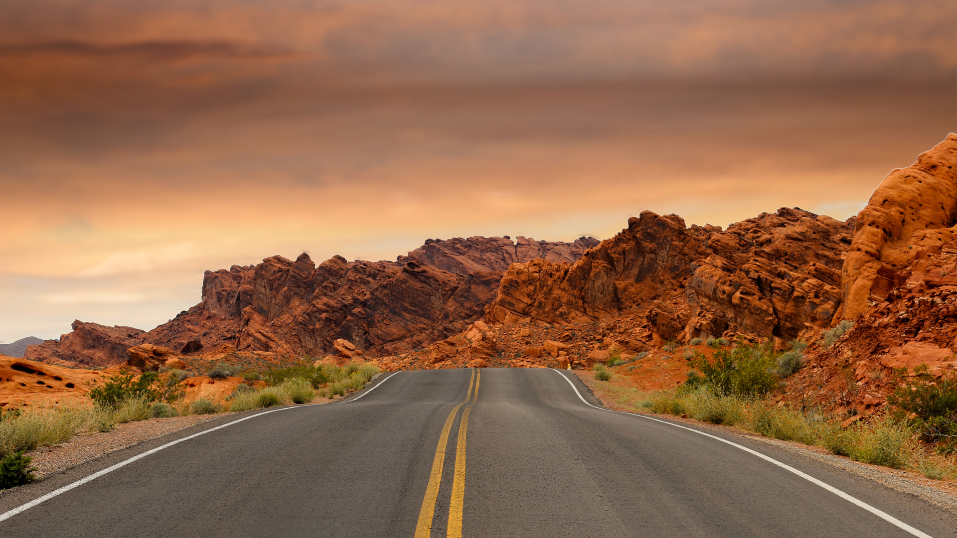 An empty road in the desert with mountains in the background.