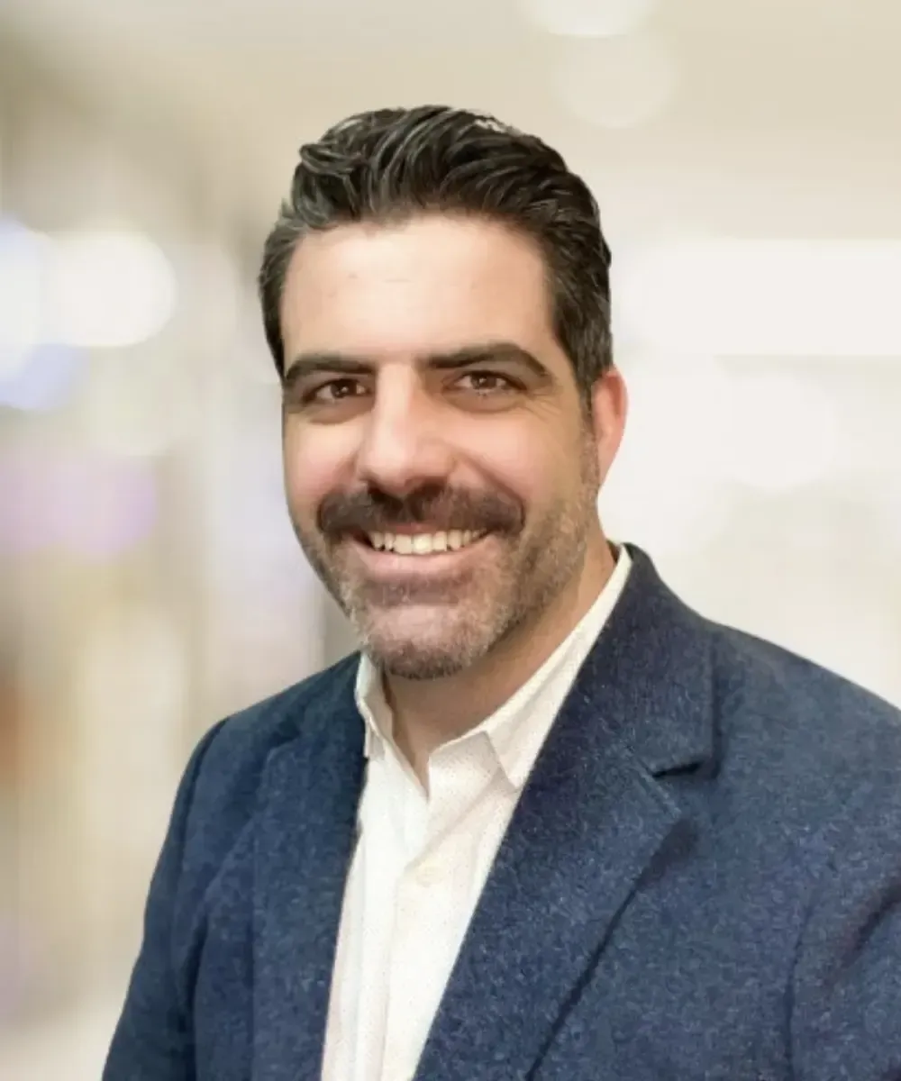 A man with a beard wearing a blue jacket and white shirt is smiling for the camera.