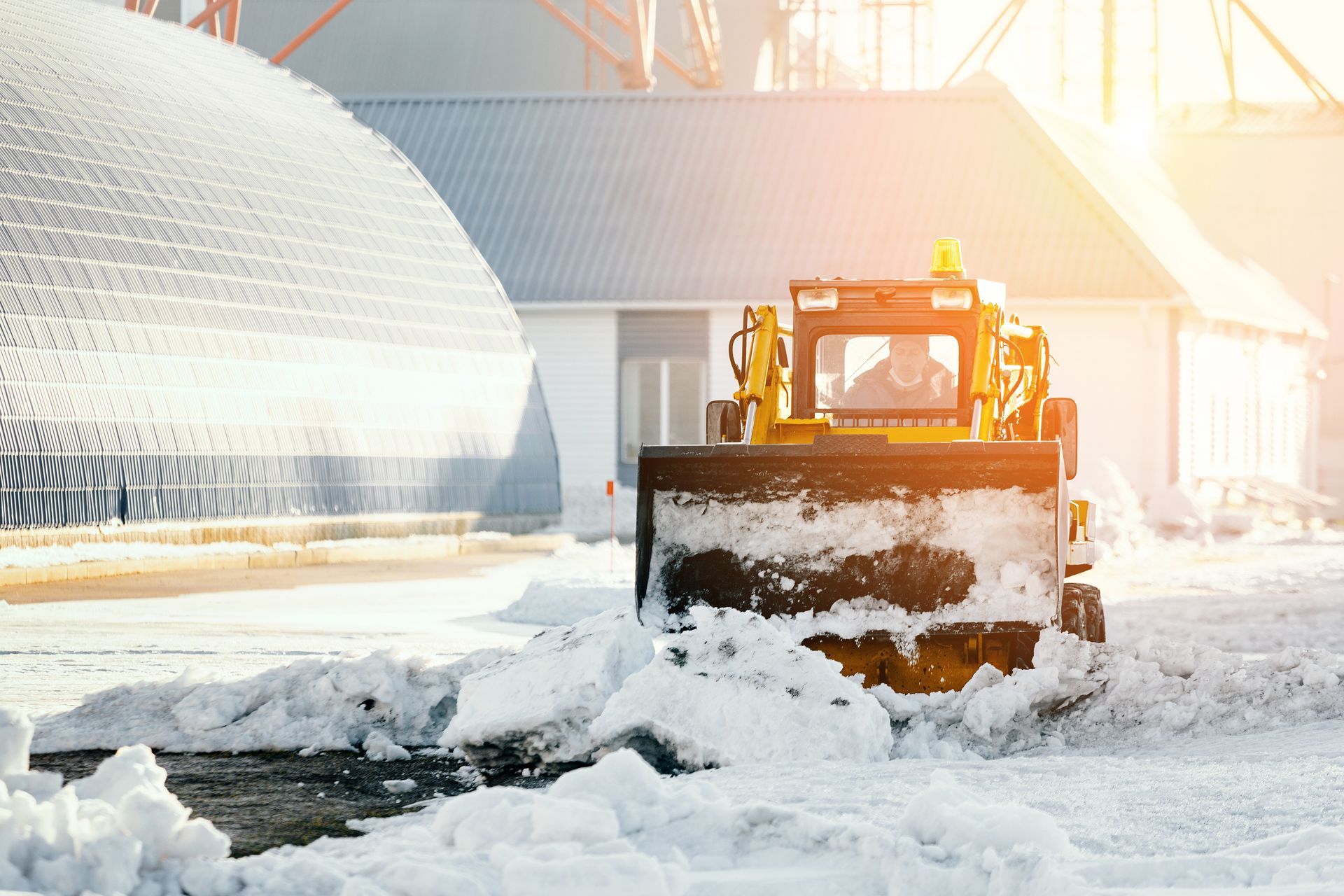 A snow plow is clearing snow from a parking lot in front of a building.