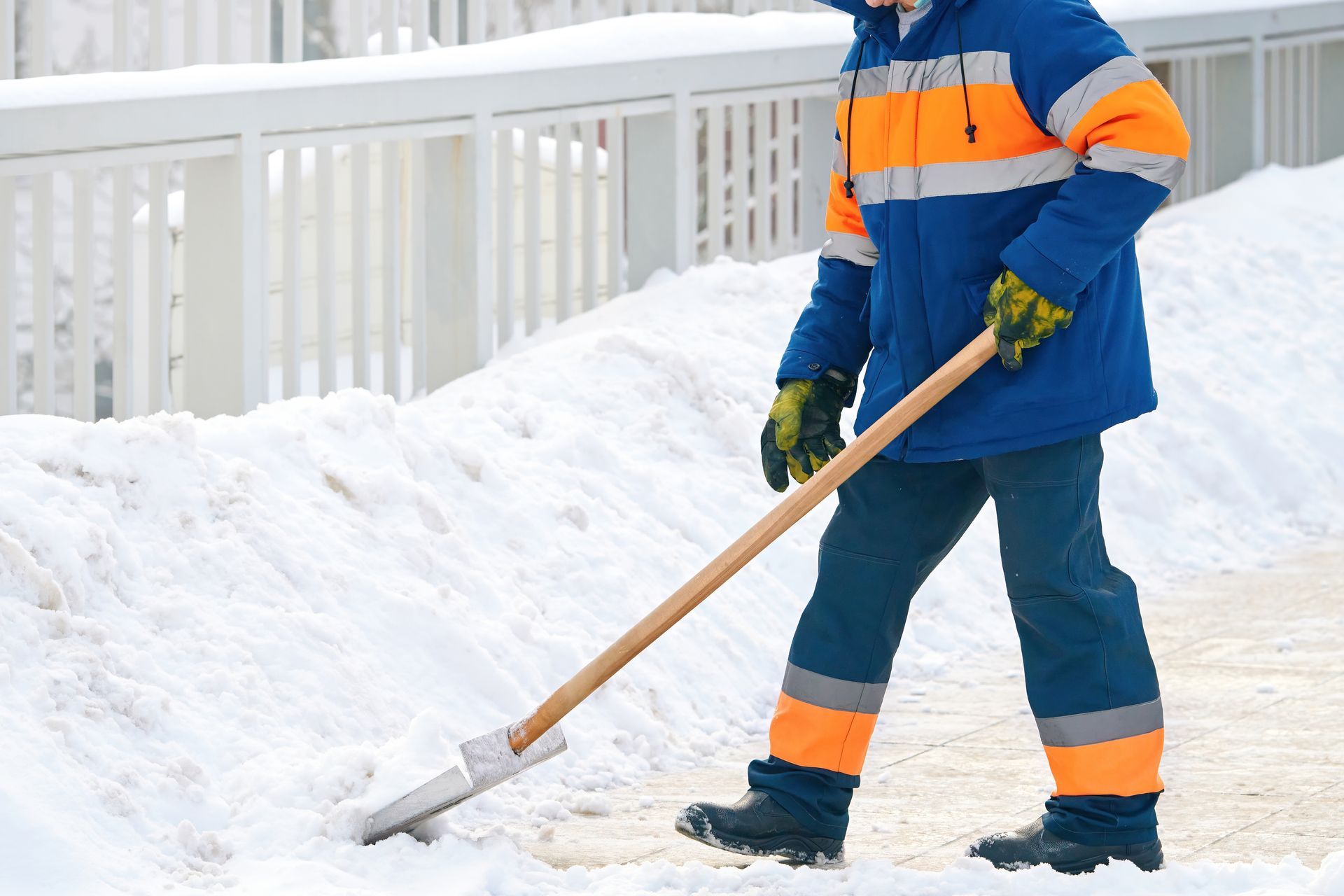 A man in a blue and orange jacket is shoveling snow.