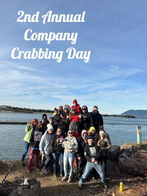 Group of people posing by water, celebrating 2nd Annual Company Crabbing Day. Blue sky, partly cloudy.